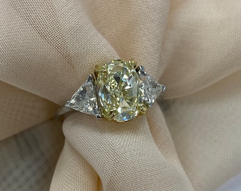 Pode incluir: Um anel de noivado de diamante amarelo com dois diamantes triangulares menores de cada lado. O anel é engastado em ouro branco e tem uma banda de ouro amarelo.