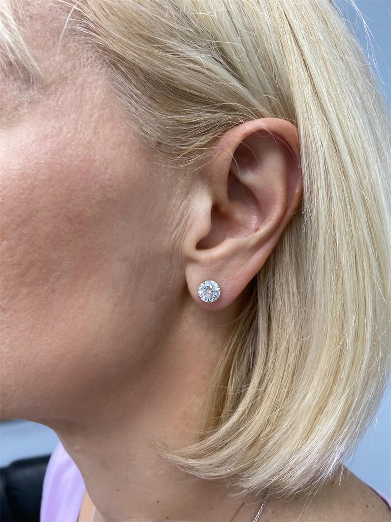 May include: A pair of silver stud earrings with a round, clear stone in the center. The stones are surrounded by a halo of smaller, clear stones.