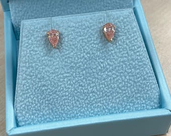 May include: A pair of pink pear-shaped stud earrings set in gold, displayed in a light blue jewelry box. The earrings have a delicate, feminine design, perfect for adding a touch of elegance to any outfit. The box provides a secure and stylish presentation.