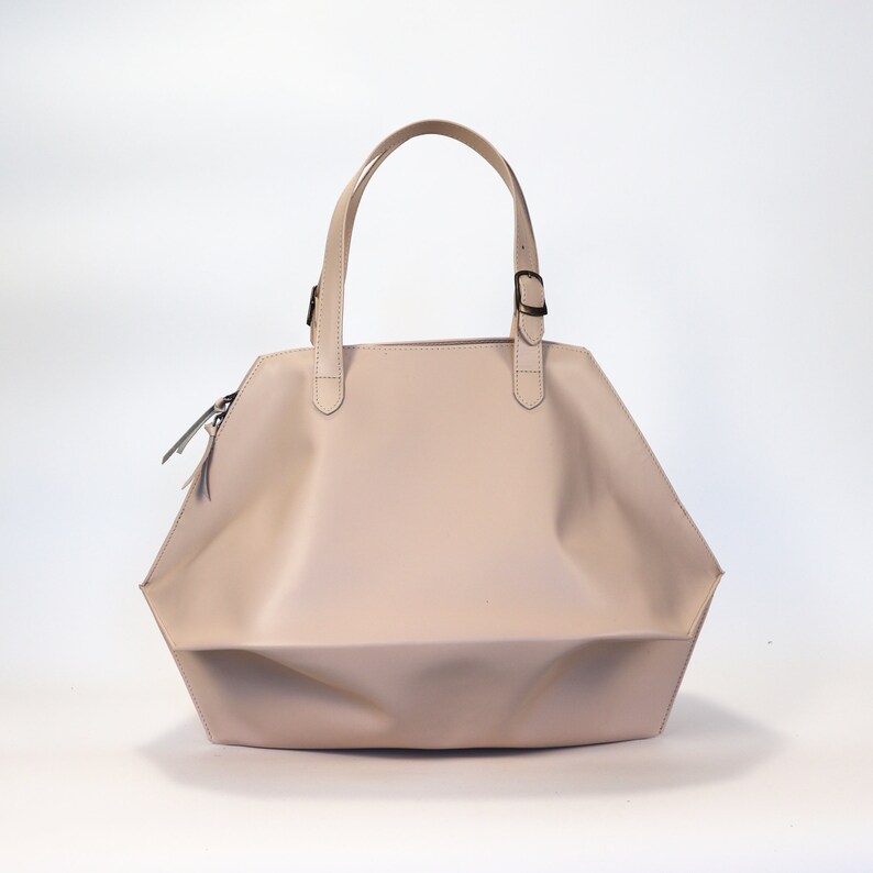 May include: A light pink leather tote bag with a single top handle and a buckle closure.