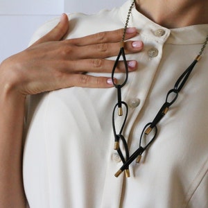 May include: A black leather necklace with gold accents. The necklace features a series of loops and is worn by a person with a white shirt.