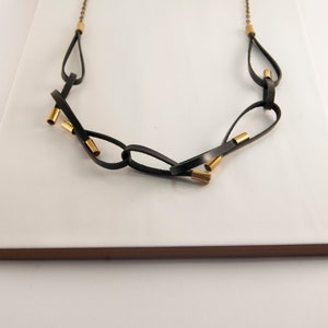 May include: A black leather necklace with gold accents. The necklace is made of multiple loops of leather that are connected by gold rings.
