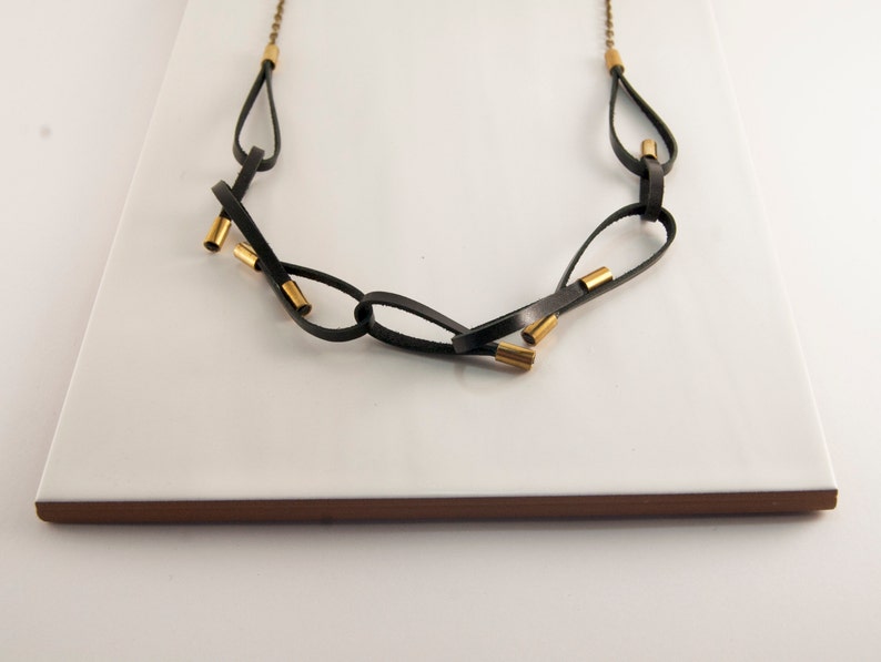 May include: A black leather necklace with gold accents. The necklace is made of multiple loops of leather that are connected by gold rings.
