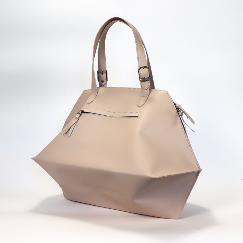 May include: A light beige leather tote bag with two top handles and a zipper closure. The bag has a geometric shape with a pointed bottom.