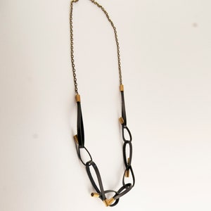 May include: A black leather necklace with gold accents. The necklace is made of a series of connected loops and features a chain at the top.