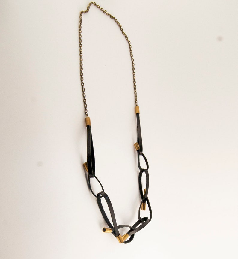 May include: A black leather necklace with gold accents. The necklace is made of a series of connected loops and features a chain at the top.