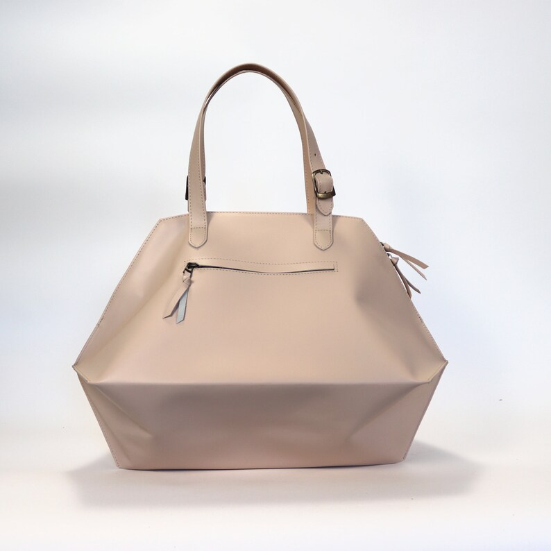 May include: A light pink leather tote bag with a zippered pocket and a buckle closure on the top handle.