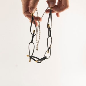 May include: A black leather necklace with gold accents. The necklace is made of multiple loops of leather connected by gold chain links.