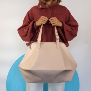 May include: A light pink leather tote bag with a buckle closure and two top handles. The bag is folded in a geometric shape.