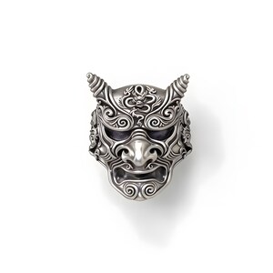 Op de afbeelding: Een gedetailleerde zilveren ring met een Japans demonenmasker ontwerp. De ring heeft ingewikkeld krulwerk, hoorns en een strenge gezichtsuitdrukking. Een uniek sieraad voor liefhebbers van bijzondere sieraden.