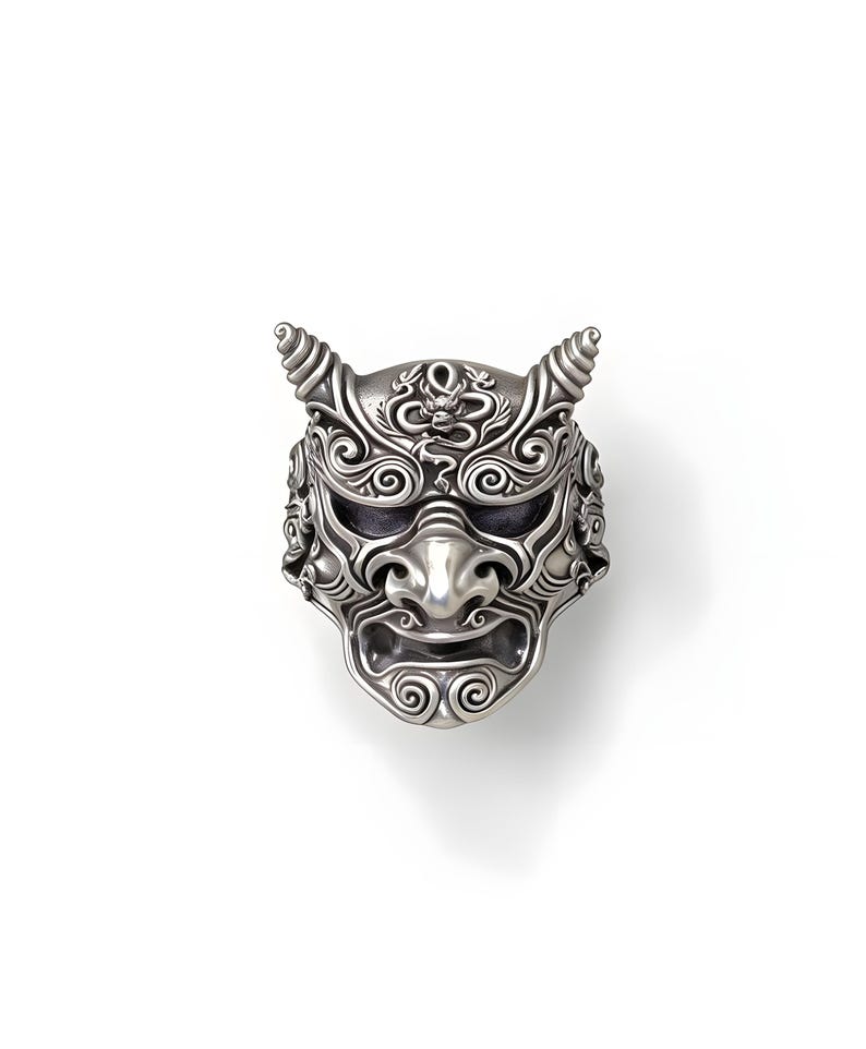 Op de afbeelding: Een gedetailleerde zilveren ring met een Japans demonenmasker ontwerp. De ring heeft ingewikkeld krulwerk, hoorns en een strenge gezichtsuitdrukking. Een uniek sieraad voor liefhebbers van bijzondere sieraden.