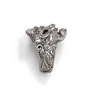 Op de afbeelding: Een gedetailleerde zilveren ring met een sierlijk ontwerp. De ring heeft wervelende patronen, bloemmotieven en een gestileerde vis. De ring staat tegen een witte achtergrond, wat de ingewikkelde details benadrukt.