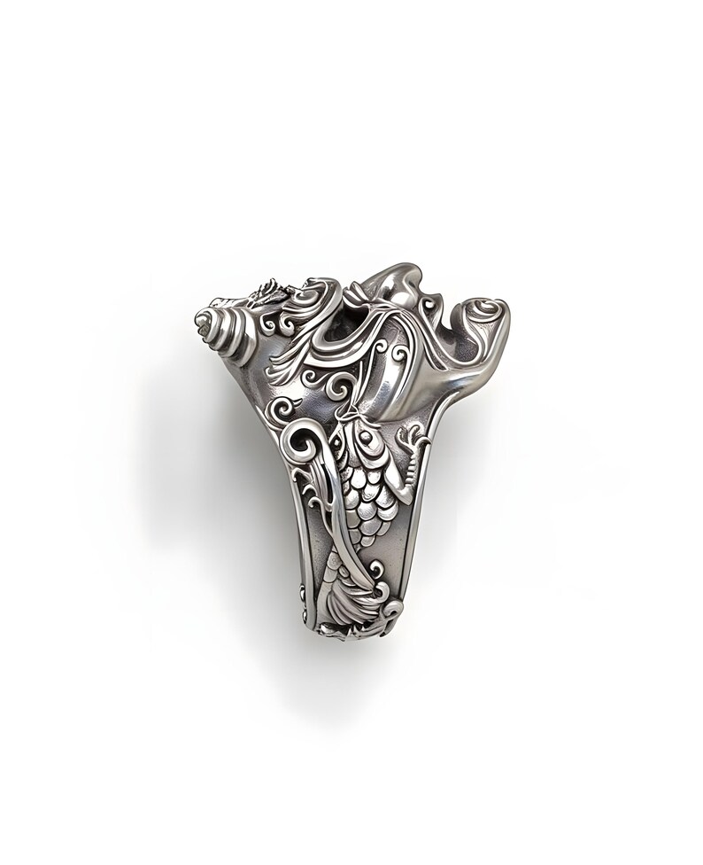 Op de afbeelding: Een gedetailleerde zilveren ring met een sierlijk ontwerp. De ring heeft wervelende patronen, bloemmotieven en een gestileerde vis. De ring staat tegen een witte achtergrond, wat de ingewikkelde details benadrukt.