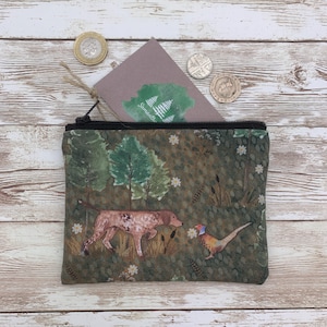 May include: A green canvas zippered pouch with a woodland scene featuring a dog, a pheasant, and trees. The pouch has a white zipper and a white background with the word "Somerset" printed on it.