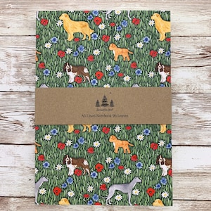 May include: A5 lined notebook with a green background featuring illustrations of various dog breeds, red poppies, and blue flowers. A brown paper band with text and a tree logo wraps around the notebook.