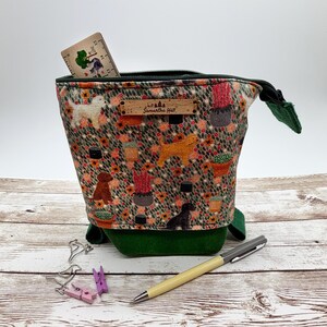 May include: A fabric pouch with a pattern of dogs and potted plants, featuring a dark green corduroy base and a zip closure. A wooden tag labelled Samantha Hall is attached to the front. A wooden ruler is tucked inside the pouch.