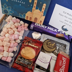 May include: A gift box filled with treats for Eid Mubarak. The box includes a chocolate bar, shortbread cookies, marshmallows, and a small card with a mosque illustration. The card reads "Eid Mubarak".