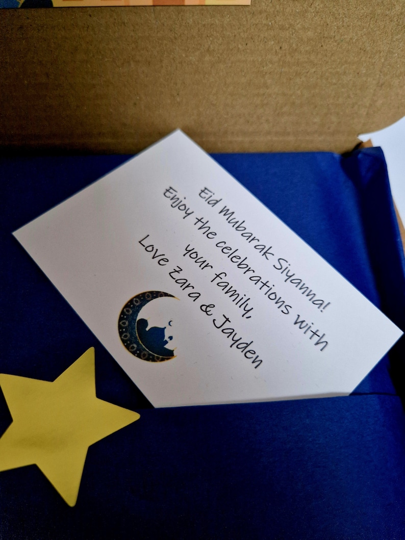 May include: A white card with a blue background and a crescent moon and star design. The card reads "Eid Mubarak Siyanna! Enjoy the celebrations with your family, Love Zara & Jayden".