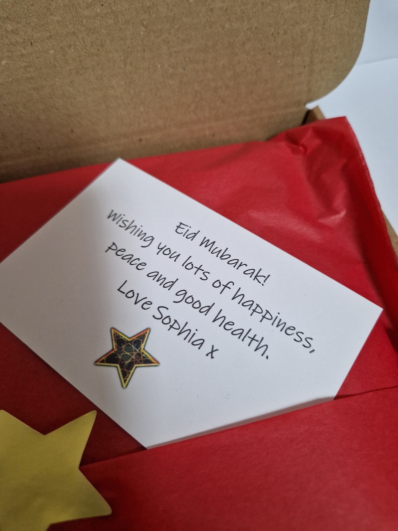 May include: A white card with a handwritten message wishing someone a happy Eid Mubarak. The message includes wishes for peace, happiness, and good health. The card is decorated with a gold star.