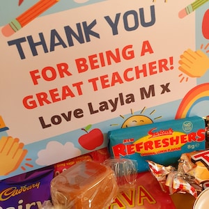 May include: A thank you card with a rainbow and a sun, with the text "Thank you for being a great teacher! Love Layla M x". The card is surrounded by various candies, including a Cadbury Dairy Milk chocolate bar, a red and yellow candy bar with the text "Swizzels Refreshers Original Lemon Flavour 8g e", and a caramel candy.