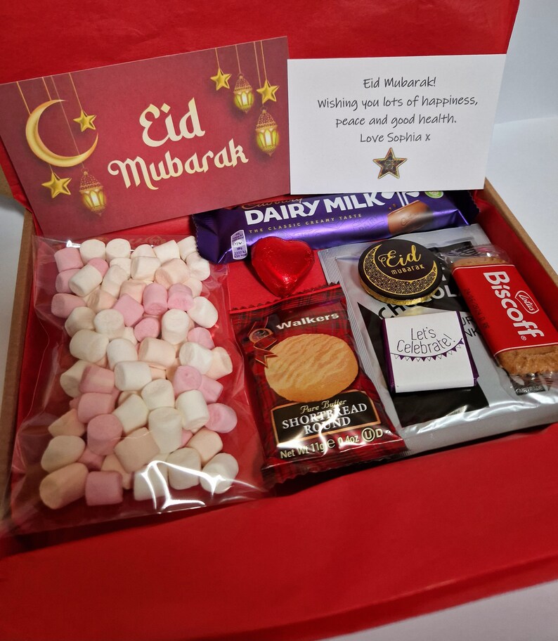 May include: A red gift box filled with treats for Eid Mubarak. The box contains a chocolate bar, a bag of marshmallows, a chocolate coin, a shortbread cookie, a biscuit, and a card with the message "Eid Mubarak! Wishing you lots of happiness, peace and good health. Love Sophia x".