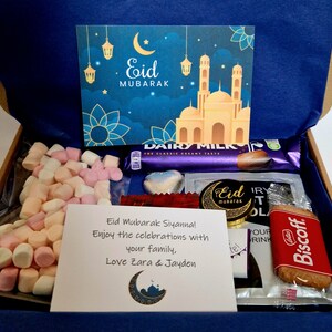 May include: A gift box filled with treats for Eid Mubarak. The box contains a card with a mosque and crescent moon, marshmallows, chocolate bars, a chocolate heart, a cookie, and a note that says "Eid Mubarak Siyanna! Enjoy the celebrations with your family, Love Zara & Jayden".