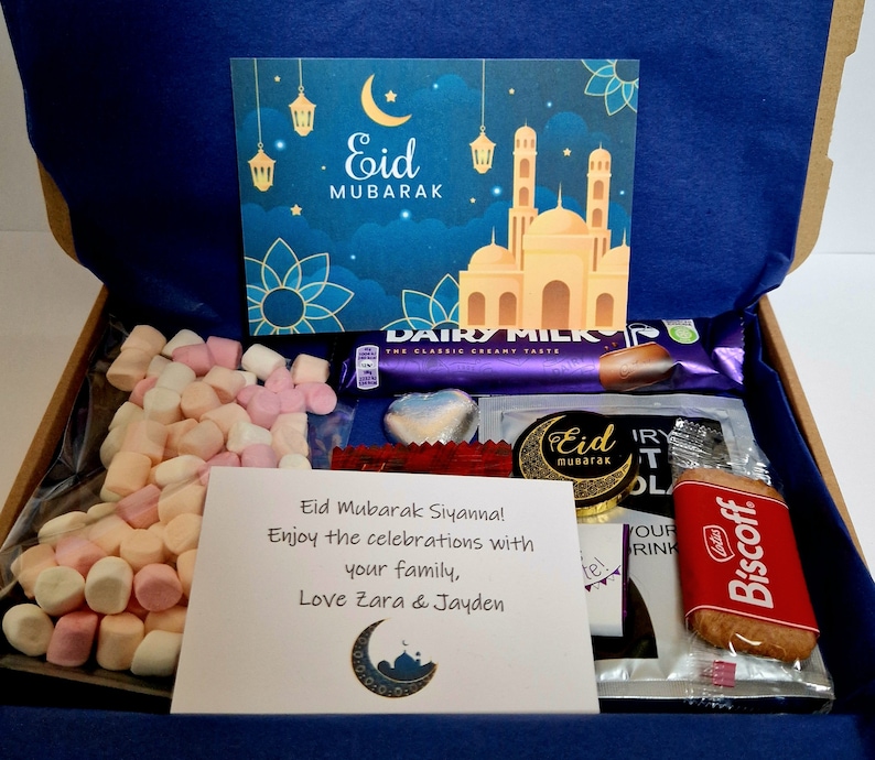 May include: A gift box filled with treats for Eid Mubarak. The box contains a card with a mosque and crescent moon, marshmallows, chocolate bars, a chocolate heart, a cookie, and a note that says "Eid Mubarak Siyanna! Enjoy the celebrations with your family, Love Zara & Jayden".