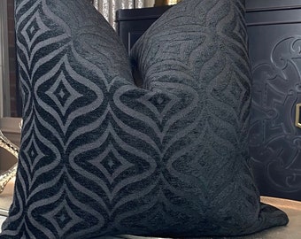 May include: Two black velvet throw pillows with a geometric pattern. The pillows are on a gray couch with a silver tray in front of them.