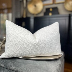 May include: A white, textured throw pillow with a subtle, raised pattern. The pillow is sitting on a silver tray.