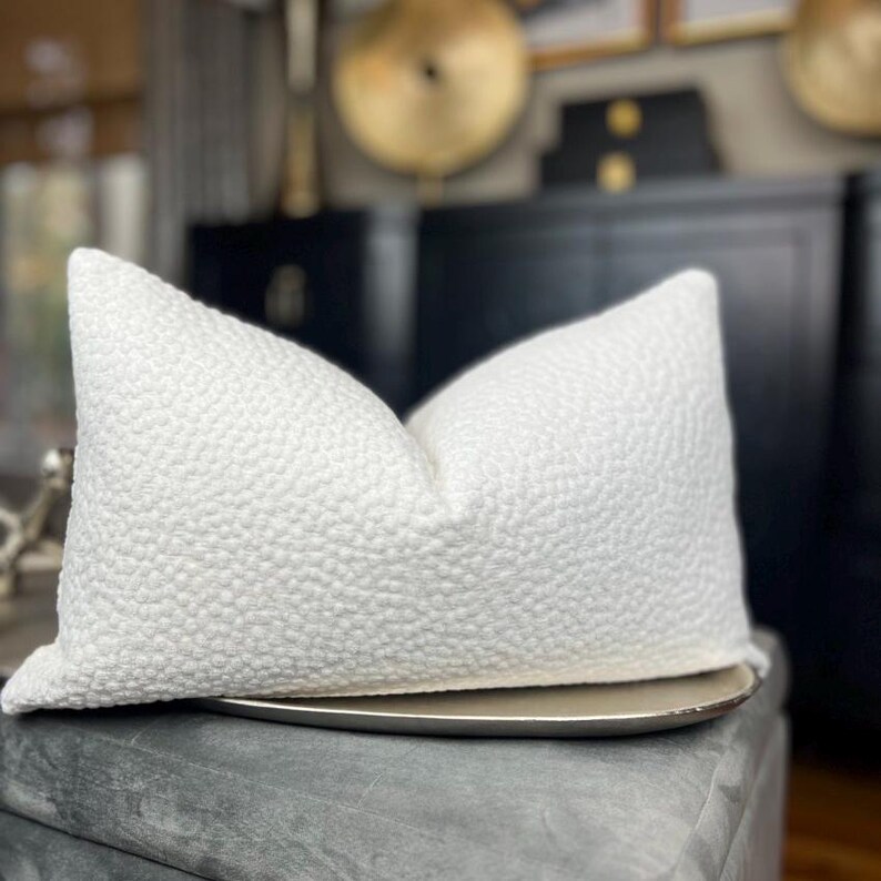 May include: A white, textured throw pillow with a subtle, raised pattern. The pillow is sitting on a silver tray.