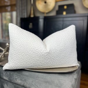 May include: White textured cushion with a subtle raised pattern. The cushion is lying on a silver tray.