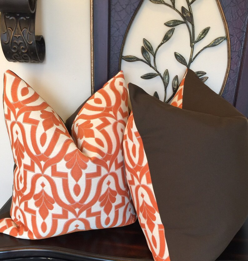 Pode incluir: Duas almofadas decorativas, uma com tecido marrom e a outra com um padr&atilde;o geom&eacute;trico branco e laranja.