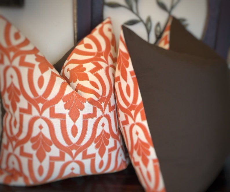 Pode incluir: Duas almofadas decorativas, uma com tecido marrom e a outra com um padr&atilde;o geom&eacute;trico branco e laranja.