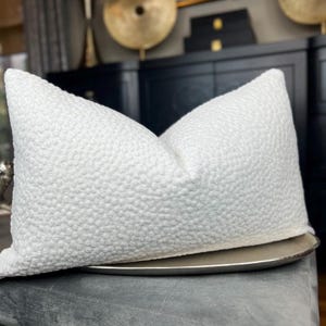 May include: White pillow with a textured, quilted surface. The pillow is sitting on a silver tray.