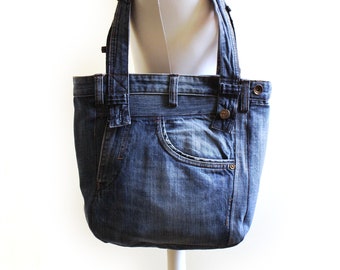 May include: A blue denim tote bag with a large pocket on the front. The bag is made from recycled jeans and has a simple design.