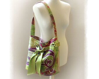 May include: A green, purple, and pink paisley patterned tote bag with a green satin ribbon bow. The bag is on a white mannequin.