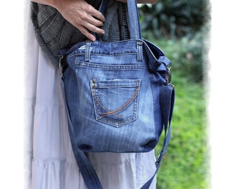 May include: A blue denim tote bag with a large pocket on the front. The bag has a long strap that can be worn over the shoulder.