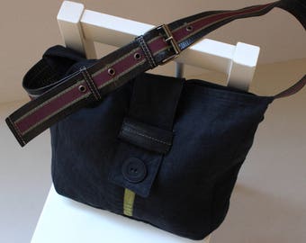 May include: A black canvas shoulder bag with a burgundy and brown striped strap. The bag has a flap with a large button and a green stripe.