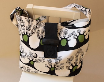 May include: A black and white tote bag with a green and black tree design. The bag has a black strap and a black buckle.