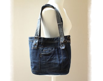 May include: A blue denim tote bag with a single pocket on the front. The bag has two straps and is displayed on a white mannequin.