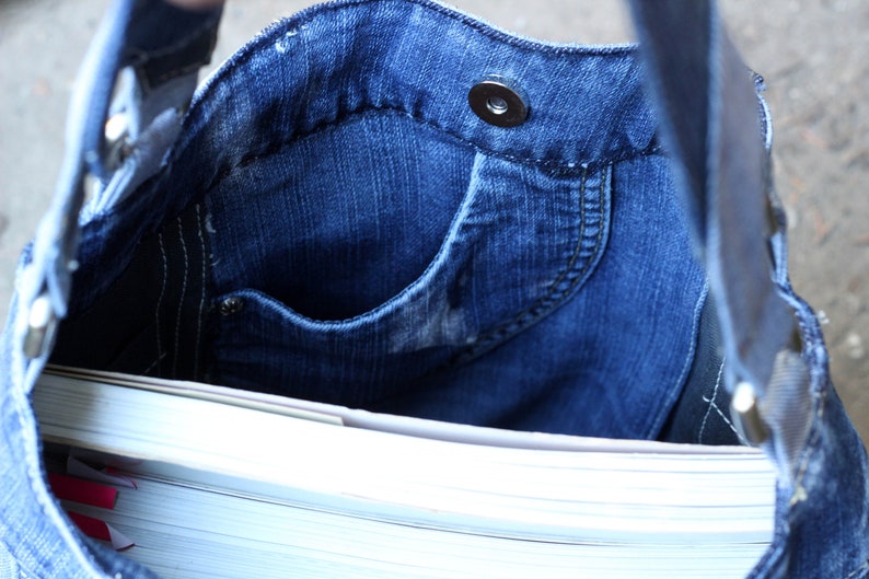 May include: A blue denim tote bag with a zipper closure and a large pocket on the front. The bag is open and filled with white paper.