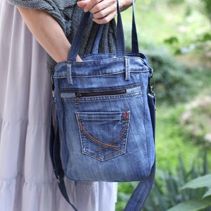 May include: A denim tote bag with a zippered pocket and a large front pocket. The bag has a long strap that can be worn over the shoulder.