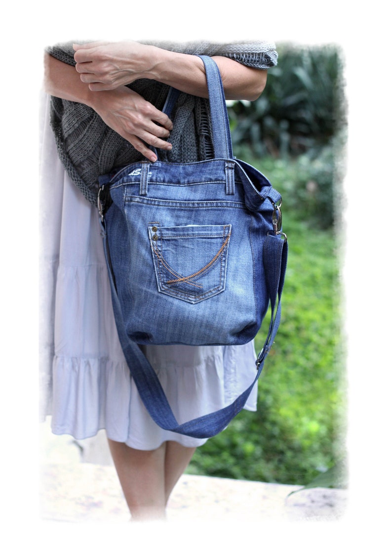 May include: A blue denim tote bag with a large pocket on the front. The bag has a long strap that can be worn over the shoulder.