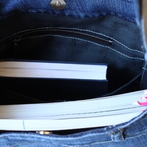May include: A blue denim tote bag with a zippered pocket and a white book inside. The bag is open and the book is visible.