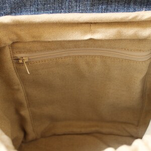 May include: The inside of a beige canvas backpack with a zippered pocket. The backpack has a denim flap.