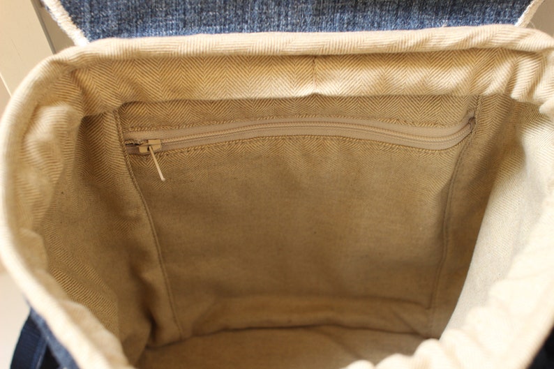 May include: The inside of a beige canvas backpack with a zippered pocket. The backpack has a denim flap.