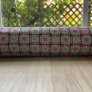 May include: Red and green fabric with a snowflake pattern. The fabric is folded into a roll.