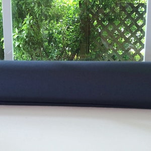 May include: A dark blue window draft stopper made of fabric. The stopper is placed on a white surface.