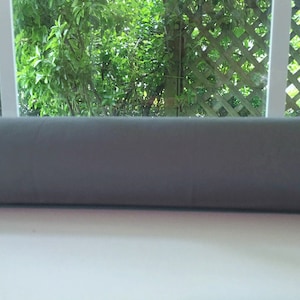 May include: A gray window draft stopper, a long, cylindrical tube made of fabric, is placed on a windowsill.
