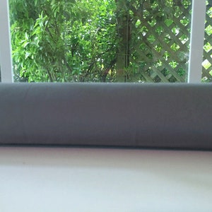 May include: A gray window draft stopper, a long, cylindrical tube made of fabric, is placed on a windowsill.